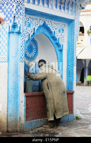 Mann trinkt aus einem Wasserbrunnen in Chefchaouen, Marokko Stockfoto