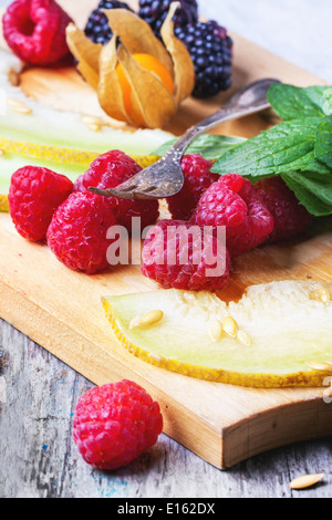 Mischung aus Himbeeren, Brombeeren, Minze, Physalis und Melone auf Holzbrett über Holztisch. Stockfoto