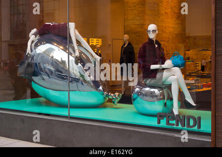 Manhattan, New York, USA - 21. Mai 2014 - In the Fendi 5th Avenue Store Schaufenster, Schaufensterpuppen tragen braune Kleider und Schuhe sitzen auf und in Rückenlage liegend, große Strukturen ähnlich Silber Mylar Luftballons, NYC. Eine Fendi Handtasche braun Leder hängt aus einer Hand. Stockfoto