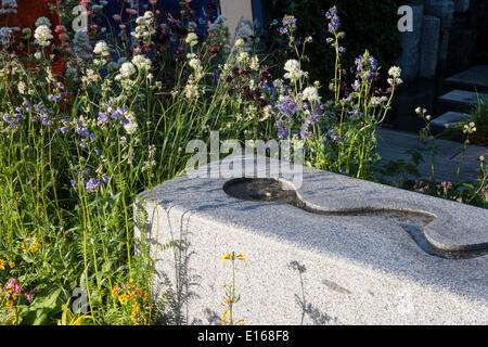 Im Garten herrliches Wasser auf einem Felsbrocken mit Blumenbeet Blumen im Frühjahr Großbritannien Stockfoto