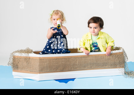 Kleine Mädchen und jungen (2-3, 12-23 Monate) sitzt im Karton Boot Spielzeug Fernrohr durchsehen Stockfoto