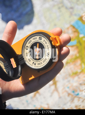 Offenen Kompass Spiegel Abdeckung in die Handfläche eines Mannes auf dem Hintergrund der topographischen Karten liegen. Stockfoto