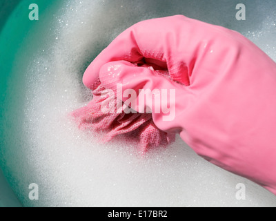 Hand in rosa Gummihandschuh nasses Tuch im schäumenden Wasser spülen Stockfoto