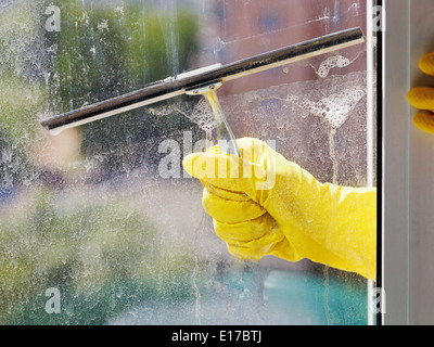 Hand in gelben Handschuh reinigt nach Hause Fensterglas durch Rakel im Frühling Stockfoto