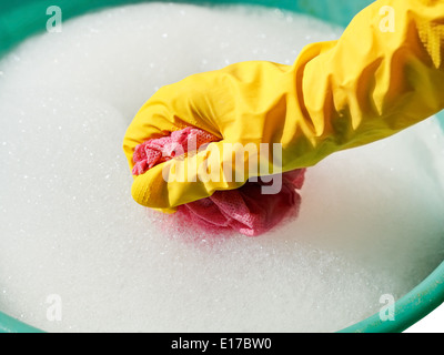 Hand im gelben Gummihandschuh nasses Tuch im schäumenden Wasser spülen Stockfoto