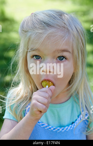 Kleine Kind blondes Mädchen lecken Lutscher draußen im Garten, portrait Stockfoto