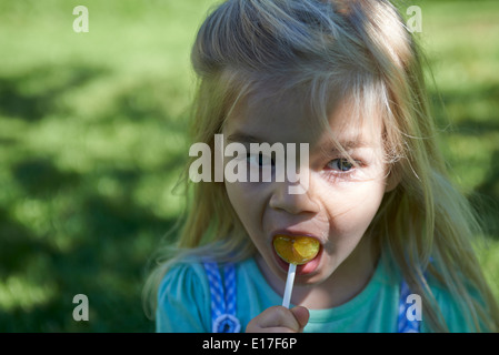 Kleine Kind blondes Mädchen lecken Lutscher draußen im Garten, portrait Stockfoto