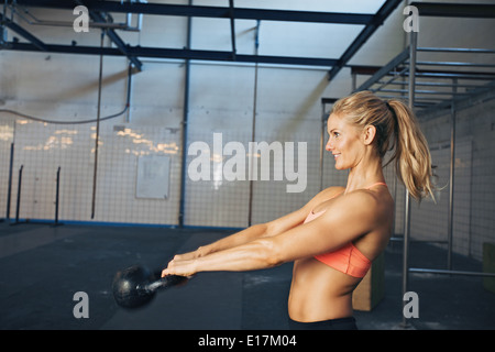 Seitenansicht der glückliche junge Frau mit Wasserkocher Glocke im Fitnessraum trainieren. Kaukasische Sportlerin Crossfit Training im Fitness-Studio zu tun. Stockfoto