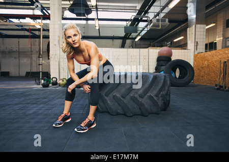 Passen Sie die junge Dame sitzt auf einem großen Reifen nach ihrem Training. Frau Rast nach dem Training im Fitnessraum. Stockfoto