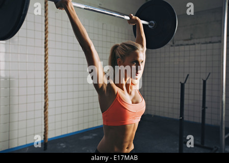 Starke Frau heben Langhantel als Teil von Crossfit Routine-Übung. Passen Sie die junge Frau Heben schwerer Gewichte im Fitnessstudio. Stockfoto