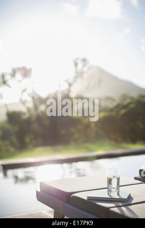 Wasserglas und Buch auf der Sonnenliege am sonnigen Pool Stockfoto