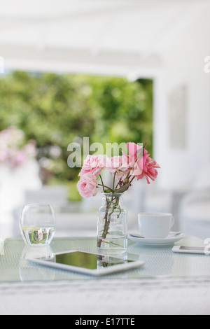 Rosa Rosen auf Terrassentisch neben Kaffeetasse und digital-Tablette Stockfoto