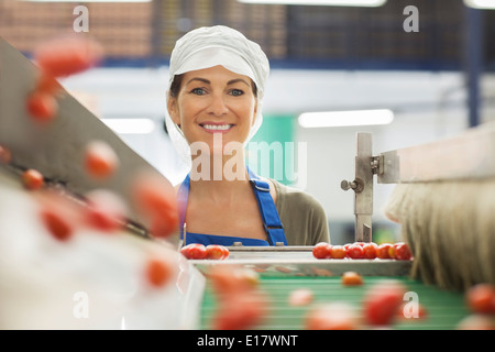 Porträt der lächelnde Arbeiter Prüfung Tomaten am Förderband in Lebensmittel verarbeitenden Anlage Stockfoto