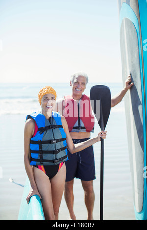 Porträt von älteres Paar mit Paddleboards am Strand Stockfoto