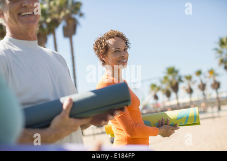 Portrait von lächelnden Frau mit Yoga-Matte am Strand Stockfoto