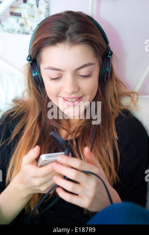 Teenager-Mädchen Musikhören mit Kopfhörer auf ihrem Iphone auf ihrem Bett im Schlafzimmer. Stockfoto