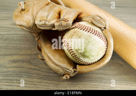 Closeup horizontale Foto eine alte schmutzige Baseball im Inneren stark beanspruchte Handschuh und hölzernen Schläger im Hintergrund auf rustikalen Holz Stockfoto