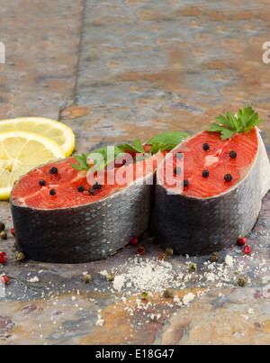 Closeup vertikale Foto von frischen roten Lachs-Steaks, Kurs Gewürzen, Kräutern und Zitronenscheiben mit natürlichen Stein Schiefer unter Stockfoto