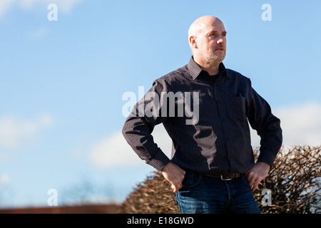 Blick von unten auf ein nachdenklicher Mann mittleren Alters sitzt auf einer Treppe starrte in die Ferne mit einem ernsten Ausdruck Stockfoto