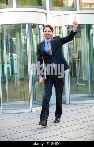 Motivierte hübscher junger Geschäftsmann verlassen seinem Bürogebäude mit einer Aktentasche unterm Arm Stanzen die Luft mit seiner Faust einen Stockfoto