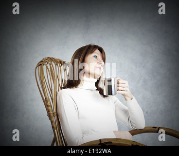 Frau in einem Sessel sitzend und mit einer Pause bei einer Tasse Kaffee oder Tee Stockfoto