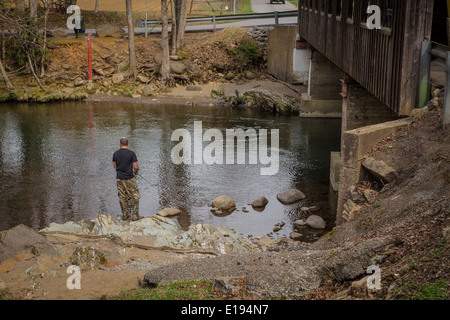 Ein Mann fischt auf Little Pigeon River, durch die Emerts Cove überdachte Brücke in Pittman Center, Tennessee Stockfoto