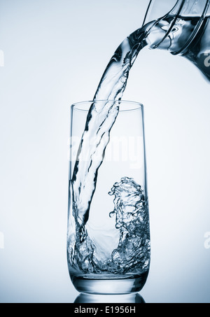 Gießt Wasser aus Glaskrug auf blauem Hintergrund Stockfoto