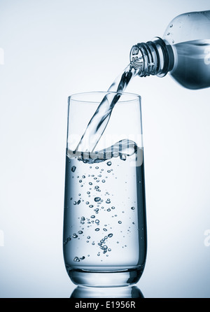 Gießen Wasser in Glas von Flasche auf blauem Hintergrund Stockfoto