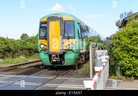 Grün und Gelb Klasse 377 Electrostar Southern Zug nähert sich einem Bahnübergang in England, Großbritannien. Südzüge. Southern Rail. Stockfoto