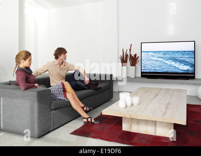 junges Paar sitzt auf dem Sofa vor dem Fernseher im Wohnzimmer Stockfoto