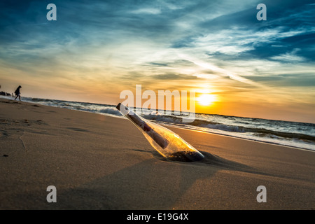 Nachricht mit Brief in der Flasche an einem Strand im Sonnenuntergang Stockfoto