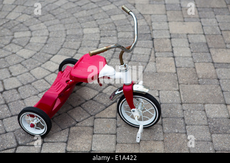 Des Kindes rot Dreirad auf einer Kopfsteinpflaster Design gepflasterte Straße geparkt Stockfoto