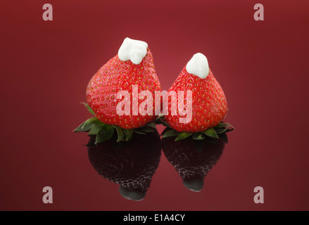 Zwei frische Erdbeeren garniert mit dicken Naturjoghurt auf rotem Grund Stockfoto