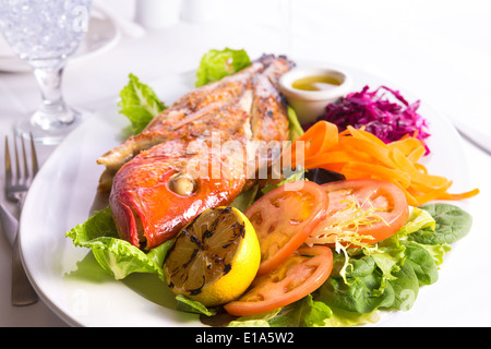 Volle gekochte Tilapia Fisch serviert in einem Teller mit Gemüse und Fisch-Sauce mit eiskaltem Wasser ergänzt Stockfoto