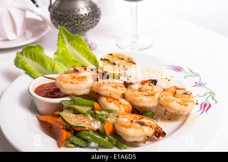 Garnelen Spieße sind gegrillte und garniert mit Gemüse und Reis serviert auf einem weißen Teller zusammen mit einem silbernen Krug Stockfoto
