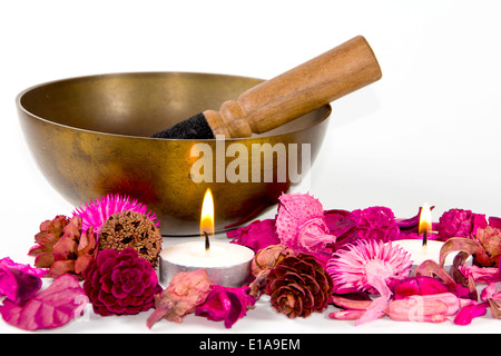 Studioaufnahme einer tibetischen Schüssel, einige rosa Blumen und Kerzen auf weißem Hintergrund. Stockfoto