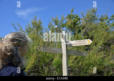 Frau, die eine Wahl der Richtung stand neben einem öffentlichen Wanderweg-Zeichen am Snow Hill, West Wittering, West Sussex, UK Stockfoto