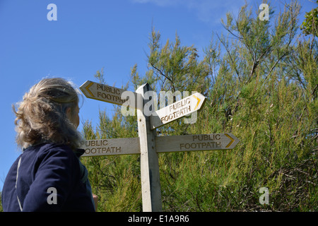 Frau, die eine Wahl der Richtung stand neben einem öffentlichen Wanderweg-Zeichen am Snow Hill, West Wittering, West Sussex, UK Stockfoto