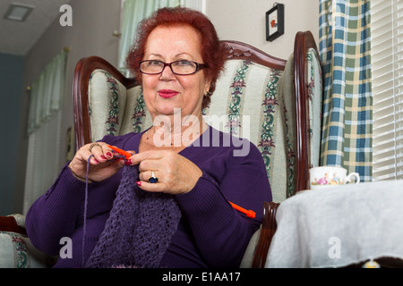 Roten Haaren senior Lady auf der Suche auf Sie mit der rechten Bewlow ihre Brille während ihren lila Schal häkeln Stockfoto