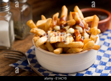 Klassische französische kanadische Poutine mit Pommes frites, Soße und Käse Quark auf einem rustikalen Tisch. Stockfoto