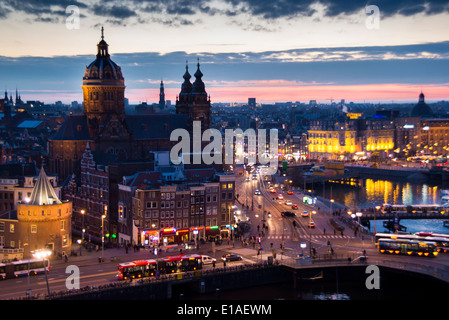 Erhöhte Ansicht von Amsterdam Bahnhofsbereich nachts mit Licht, Verkehr, Sonnenuntergang und Sint Nicolaaskerk Stockfoto