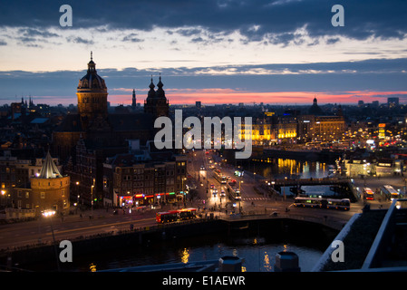 Erhöhte Ansicht von Amsterdam Bahnhofsbereich nachts mit Licht, Verkehr, Sonnenuntergang und Sint Nicolaaskerk Stockfoto