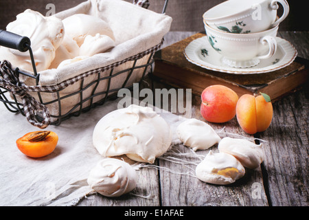 Hausgemachte Meringe, serviert mit Aprikosen und Vintage Teetassen über Holztisch. Stockfoto