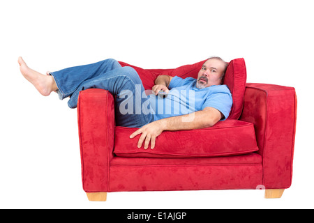 Mann in vor dem Fernseher liegen auf einem roten Sofa mit der Fernbedienung in der Hand und einen Blick von barfuß vertieft fasziniert Stockfoto