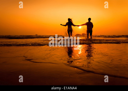 Silhouetten von paar läuft bis zum Meer am Strand bei Sonnenuntergang