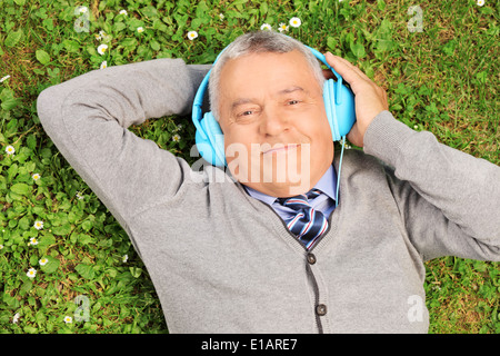 Reifer Mann mit Kopfhörern Gras auf einer Wiese liegend Stockfoto