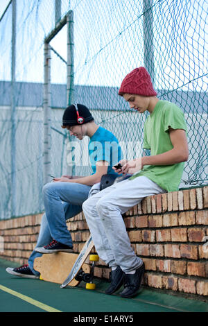 Skater sitzt auf einer Mauer, einer Musik hören, ist der andere mit Handy Stockfoto