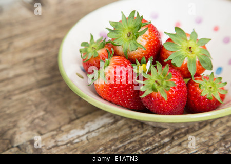 ganze Erdbeeren in gefleckte rustikale Keramikschale auf rustikalen Holztisch Stockfoto