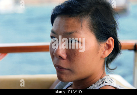 Es ist ein Foto von einer jungen chinesischen Asiatin. Sie hat kurze Haare und es ist ein Porträt. Sie sieht an der Seite. Sie liegt nahe am Meer Stockfoto