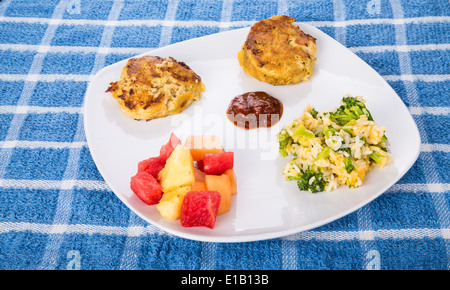 Zwei heißen Krabbenküchlein mit Cocktailsauce, Brokkoli-Käse-Reis-Auflauf und frisch geschnittene Früchte Stockfoto